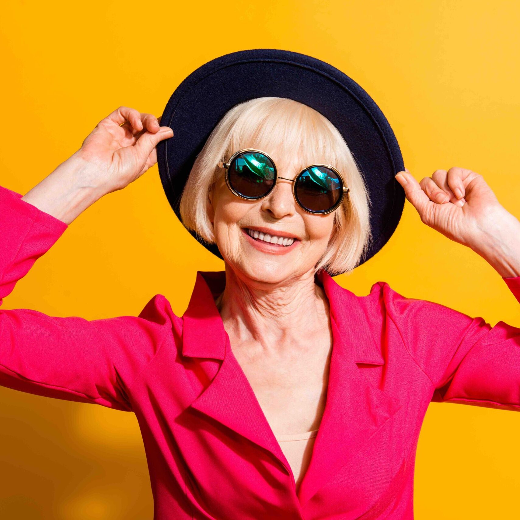 Close up portrait of fashioned old lady hold han in the hands and looking at camera isolated on yellow background